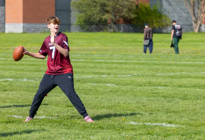 A Gow student in a maroon number 7 jersey sets to throw a football on the grass field