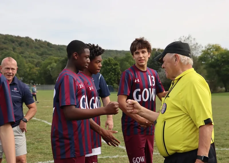 Gow soccer players in striped jerseys bump fists with the referee before a game