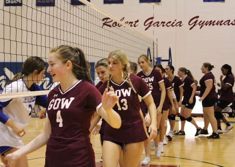 Gow volleyball players in maroon jerseys smile as they walk the handshake line after a match