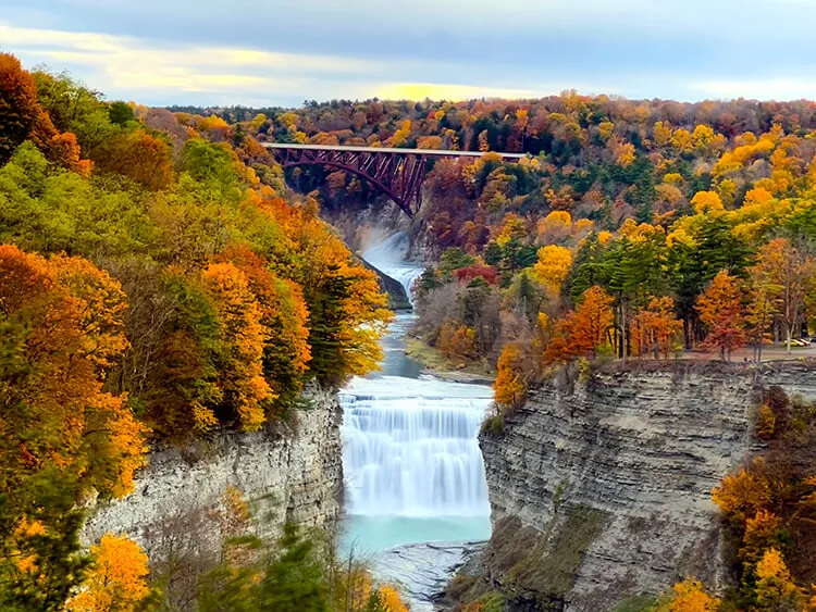 A waterfall in the Letchworth State Park gorge in fall color, with the high railroad bridge beyond