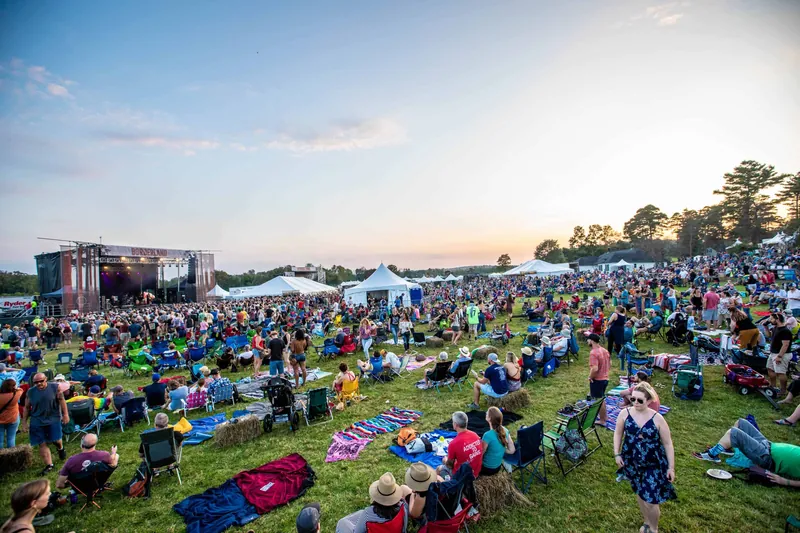 A crowd on blankets and lawn chairs at an outdoor concert at sunset
