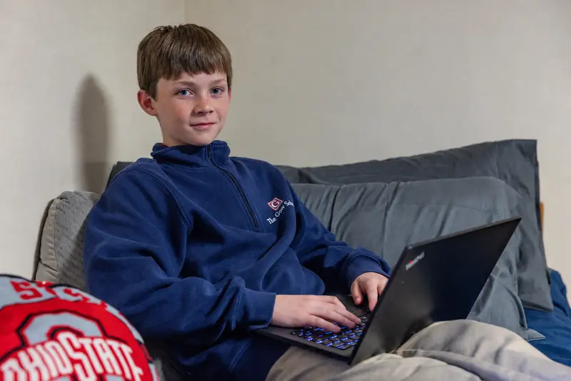 A boarding student in a Gow quarter-zip working on a laptop in his dorm room