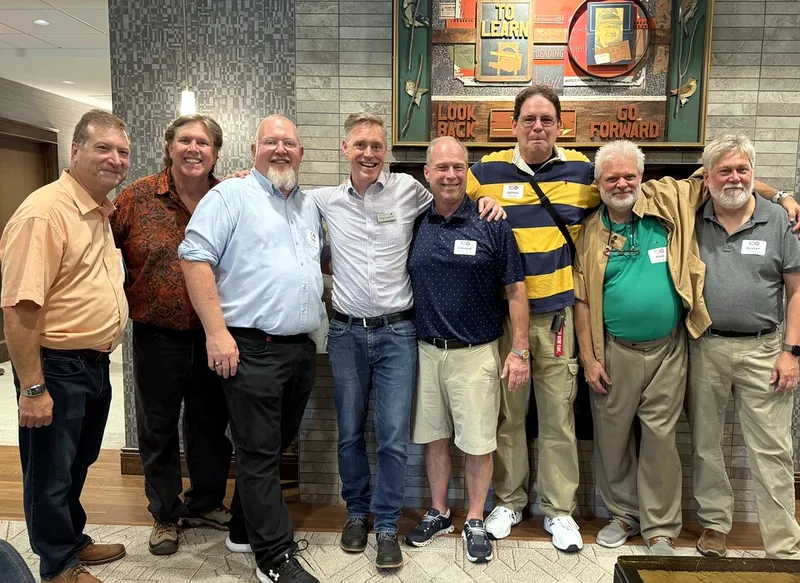 Eight alumni in centennial name tags standing together with their arms around each other