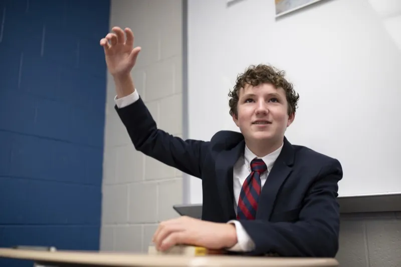 A student raises a hand in a class of four