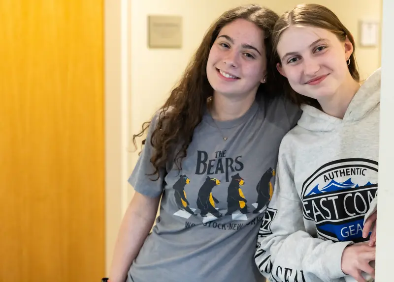 Two smiling Gow students lean together in a hallway, one in a Bears T-shirt and one in a gray hoodie