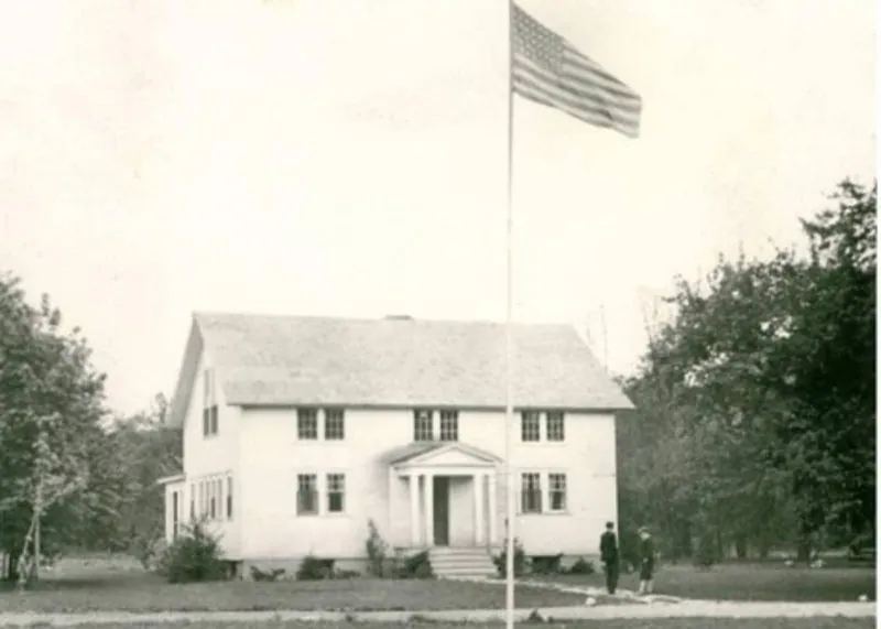Archival photograph of the Main Building, the converted horse barn, with the flag flying