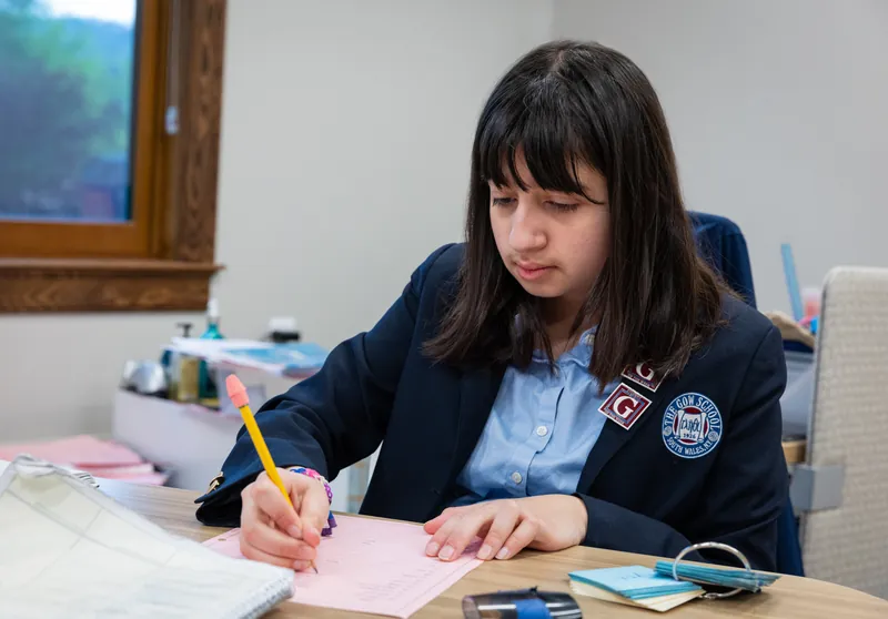 A middle school student in a Gow blazer writing with a pencil at her desk