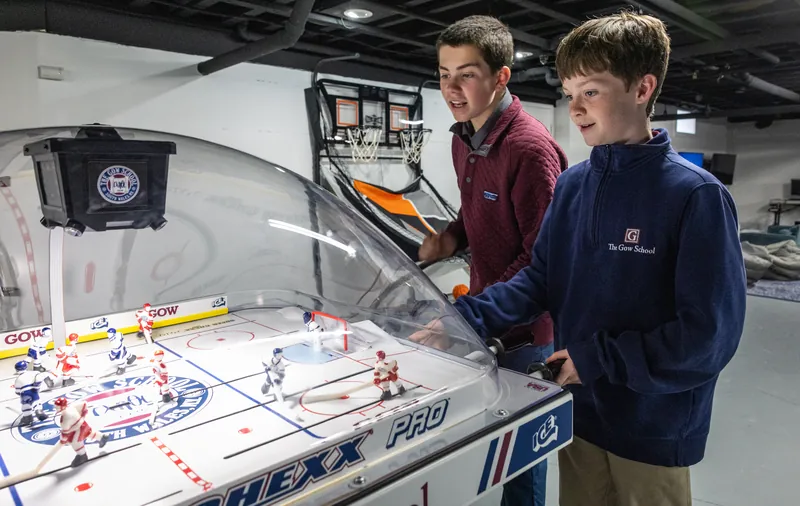 Two middle school boys playing a game of bubble hockey in a dorm common room