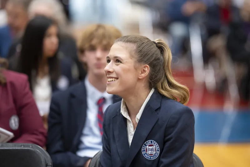 A smiling student in a Gow blazer seated among classmates at an assembly